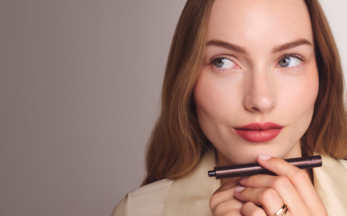 Woman wearing a warm rose lip, holding the Karen Betts pen under her chin