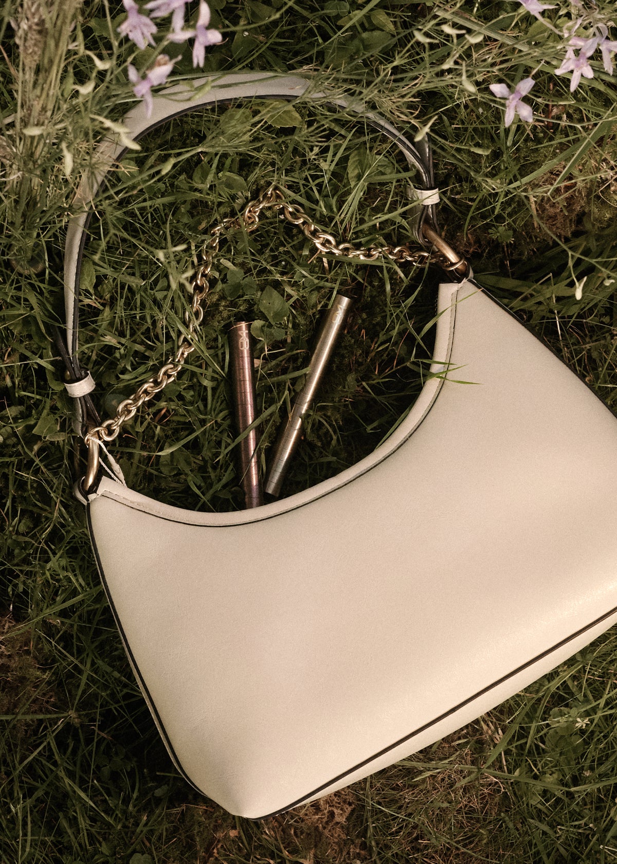 Two Karen Betts pens tucked in a white leather handbag lying in the grass