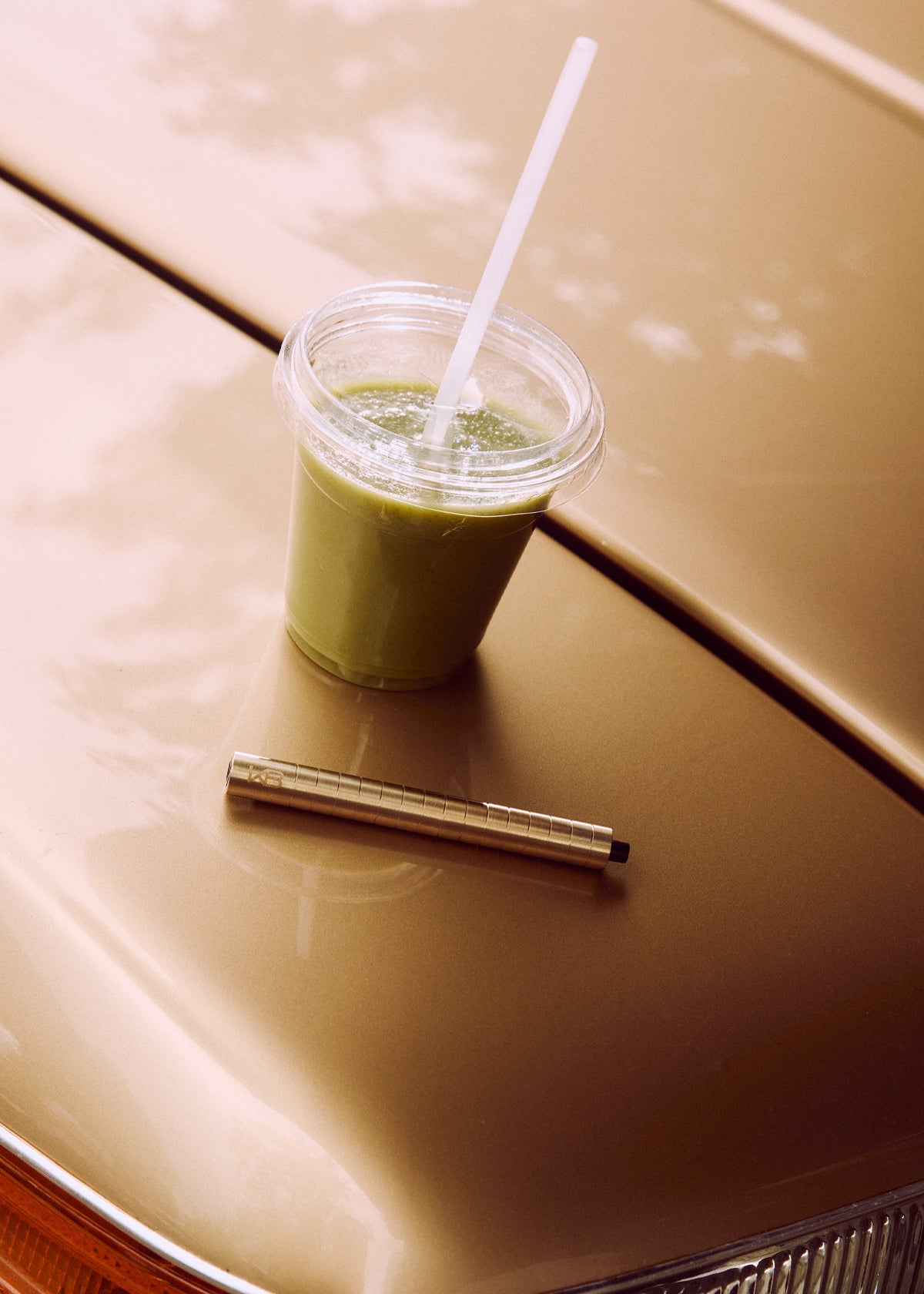 Gold-toned Karen Betts pen on a car bonnet beside a green smoothie