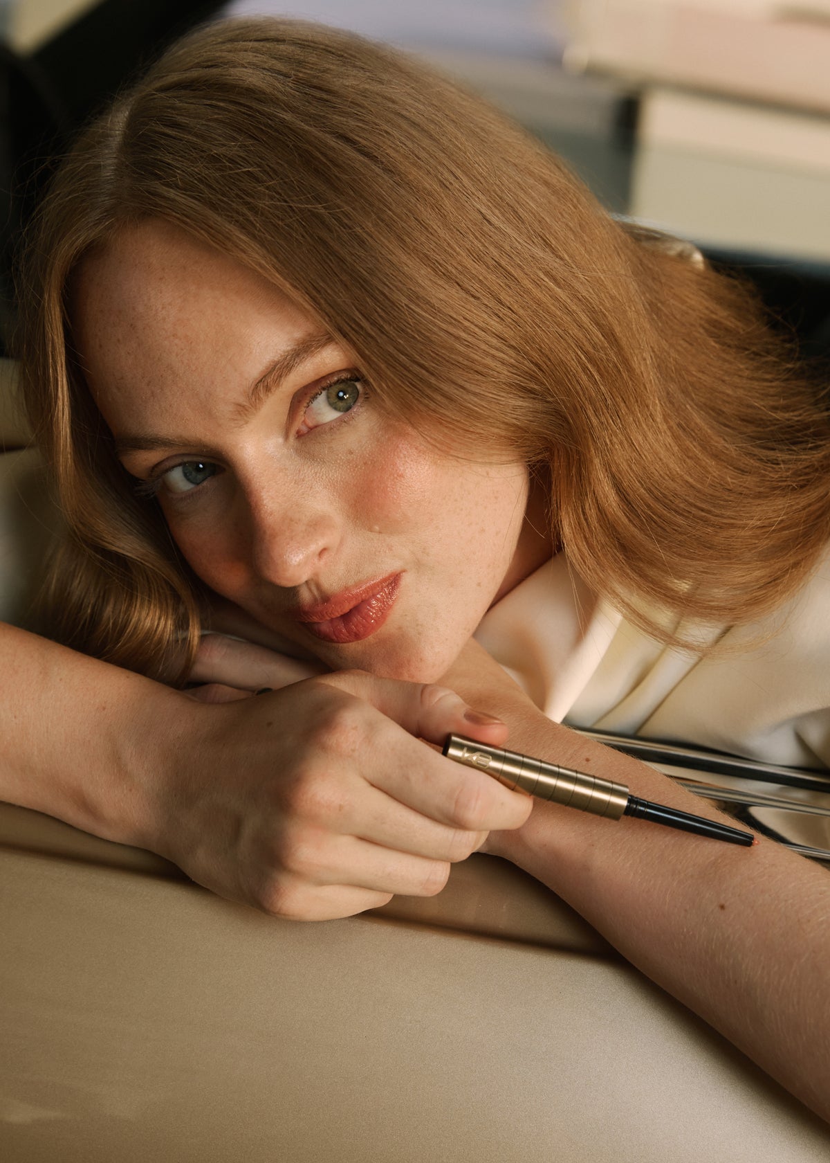 Woman resting her head on her arms, holding the Karen Betts pen, wearing a soft coral lip