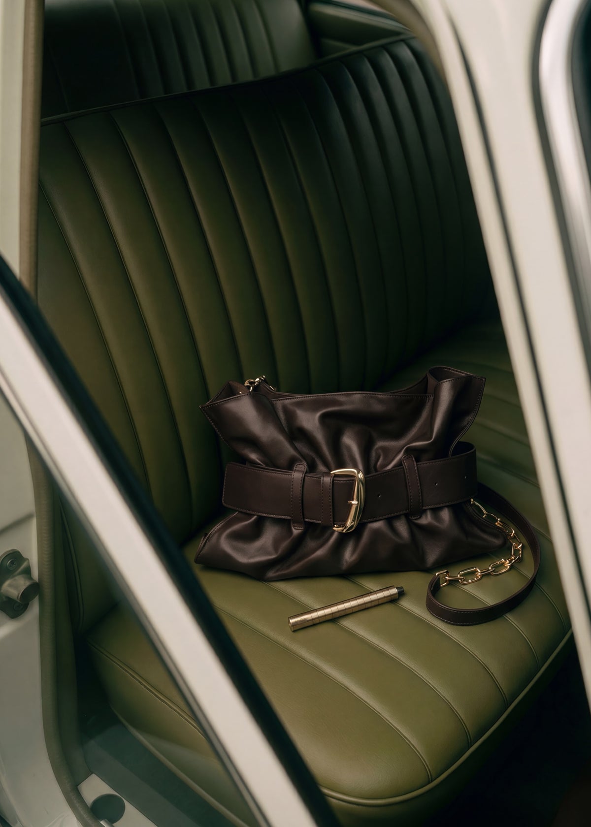 Karen Betts pen in a gold-toned finish on a green leather car seat beside a brown leather handbag
