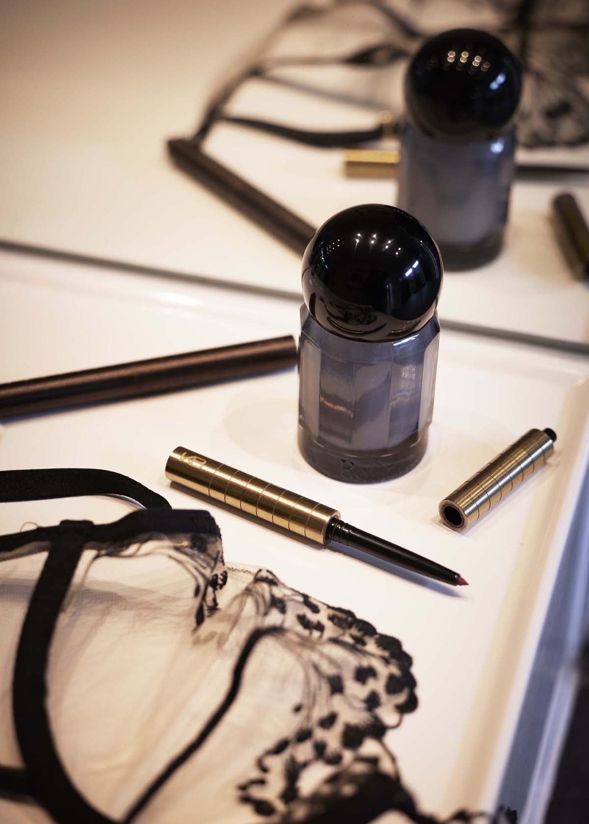 Gold-toned Karen Betts pen and lip cartridge on a dressing table beside perfume bottles and lace lingerie