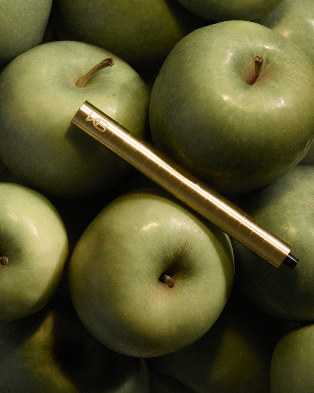 Gold-toned Karen Betts pen resting on a pile of green apples