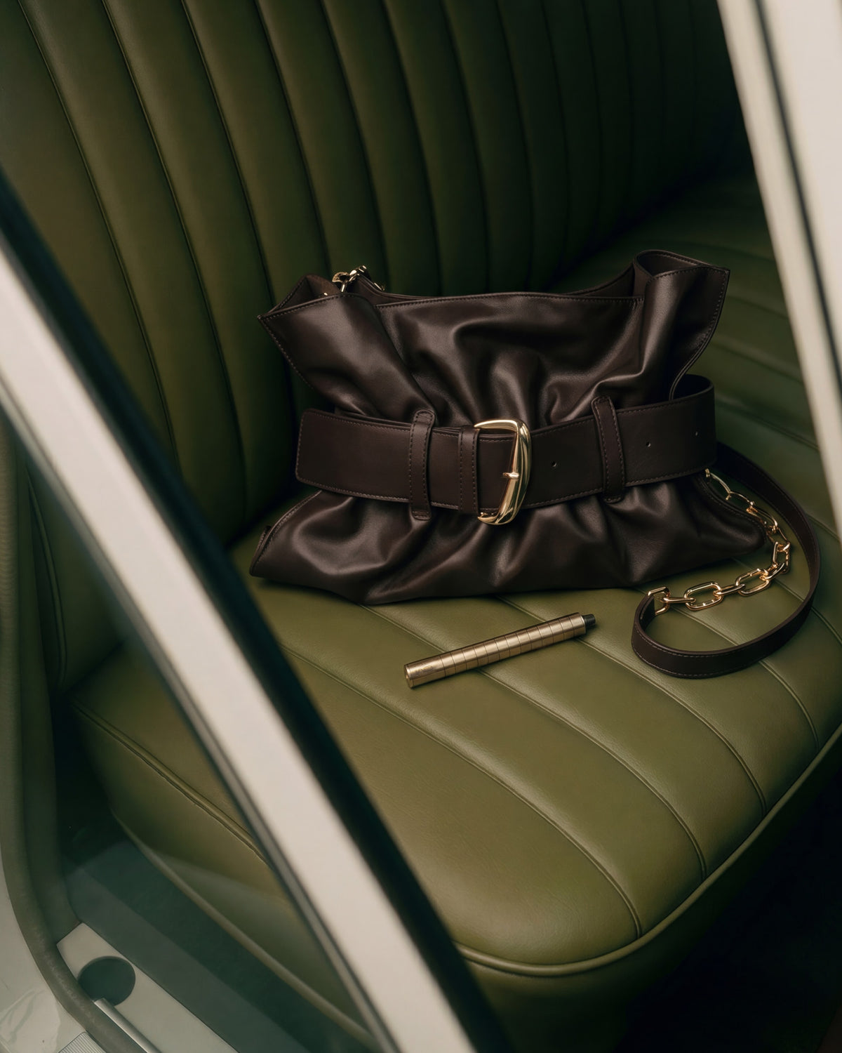 Karen Betts pen in a gold-toned finish on a green leather car seat beside a brown leather handbag
