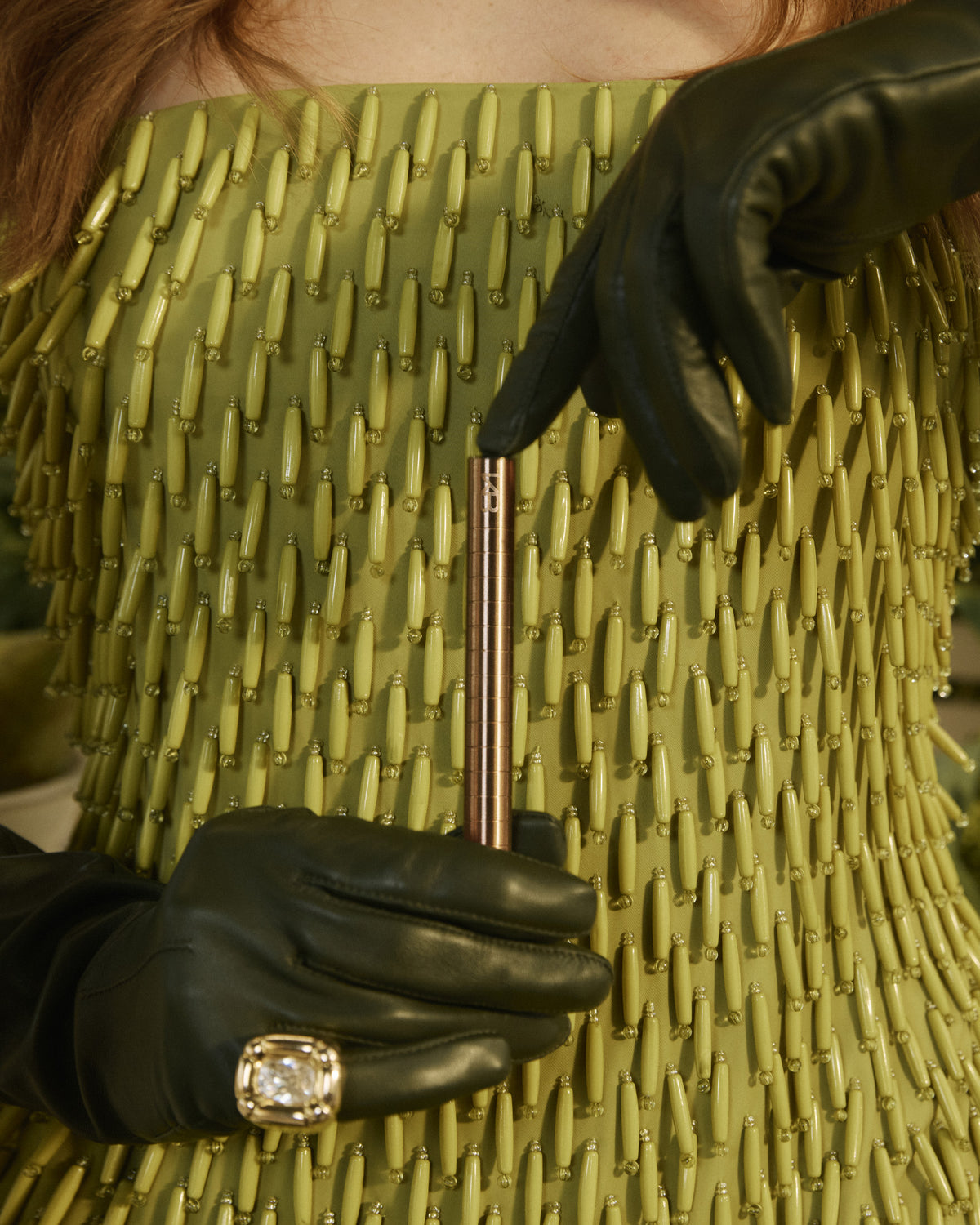 Gloved hands holding a rose-toned Karen Betts pen against a green beaded dress