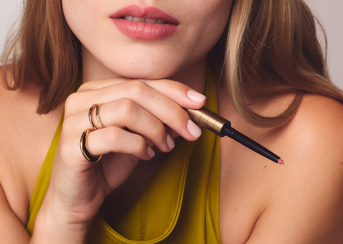 Close-up of a woman holding the Champagne Karen Betts pen with a lip cartridge, wearing a soft pink lip