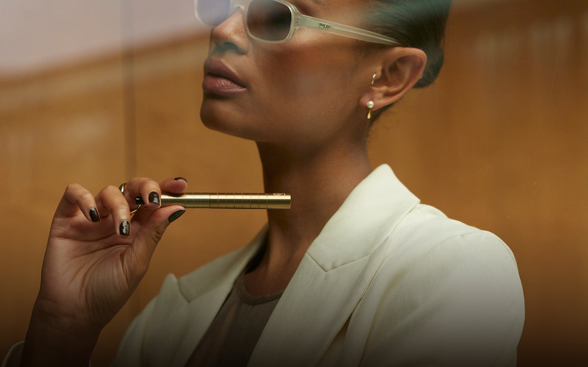 Woman in tinted glasses and a cream blazer holding a gold-toned Karen Betts pen to her chin